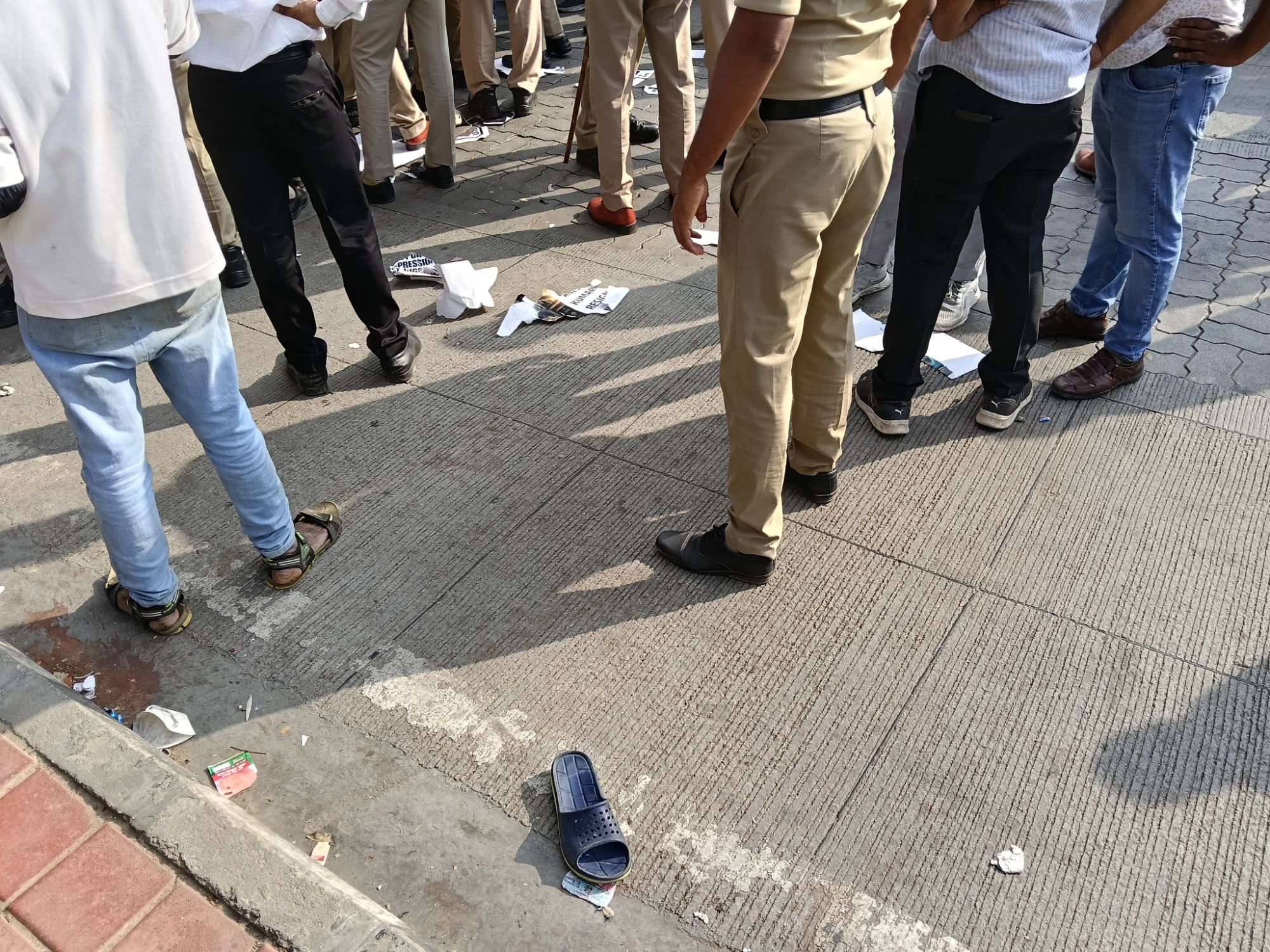 a single chappal, shreds of paper, and people's legs including a police person's